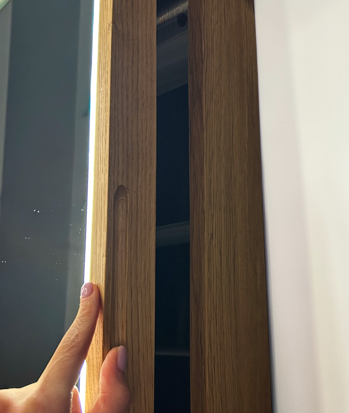 A close-up of a hand holding a light oak wood cabinet door with a recessed oval handle, showing the wood grain texture and finish.