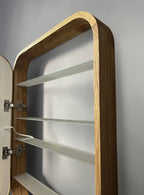 A close-up of a wall-mounted wooden cabinet or shelving unit with a curved top, three glass shelves, and visible metal hinges against a gray wall.