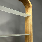 Close-up of a modern wooden shelving unit with a curved oak-look frame and two glass shelves against a dark gray background.