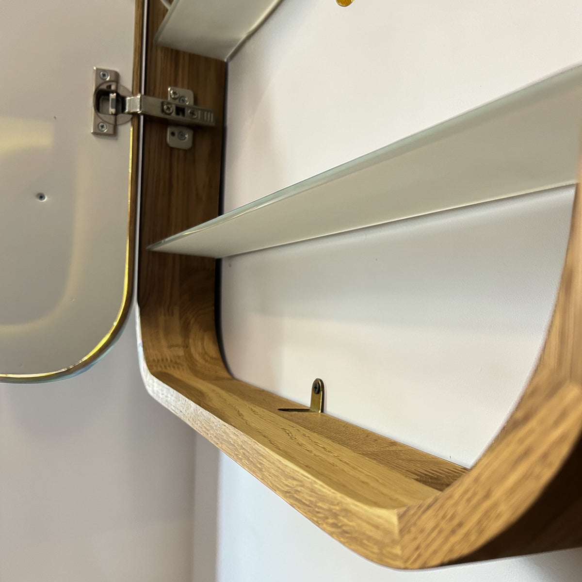 Close-up of a wall-mounted wooden medicine cabinet with a glass door, silver hinge, and interior shelf against a white wall.