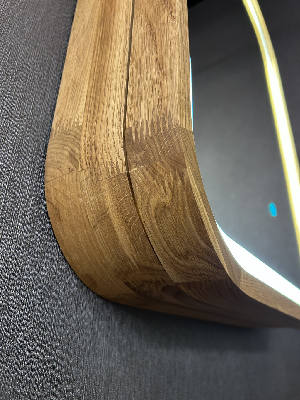 Close-up of a curved wooden frame with visible grain and scratches, resting against a dark gray textured surface.