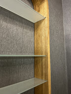 Close-up of a built-in shelving unit with three glass shelves and a light natural wood frame, set against a gray textured wall.