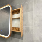 A wall-mounted bathroom cabinet with a wood grain finish, featuring two open shelves and a mirror with a white LED light frame, set against a gray tiled wall.