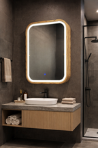 A modern bathroom vanity setup featuring a rectangular LED mirror with a light wood frame, mounted on a dark gray tiled wall above a floating wood and stone vanity cabinet with a white vessel sink.
