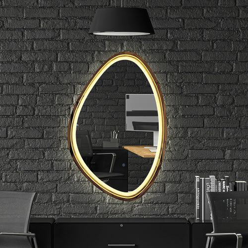 An oval wall mirror with a glowing warm gold LED frame, mounted on a dark gray brick wall above a black desk setup with a chair and a black pendant lamp.