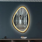 An organic-shaped LED wall mirror mounted on a dark slate blue-gray wall above a wooden console table.