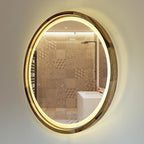 An oval wall-mounted bathroom mirror with a warm white LED light ring and a polished gold-toned frame, reflecting a tiled shower area in a bathroom.