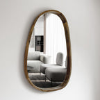 Asymmetric wood mirror reflecting a living room with an armchair