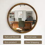 Round natural wood wall mirror with a thick rustic wooden frame, mounted on a white wall. The mirror reflects an office interior with a desk, chair, and shelves.