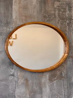 An oval wall mirror with a natural wood frame, mounted on a textured gray concrete wall.