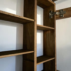 Close-up of a dark brown wooden shelving unit with multiple shelves and a metal hinge attached to a white wall.
